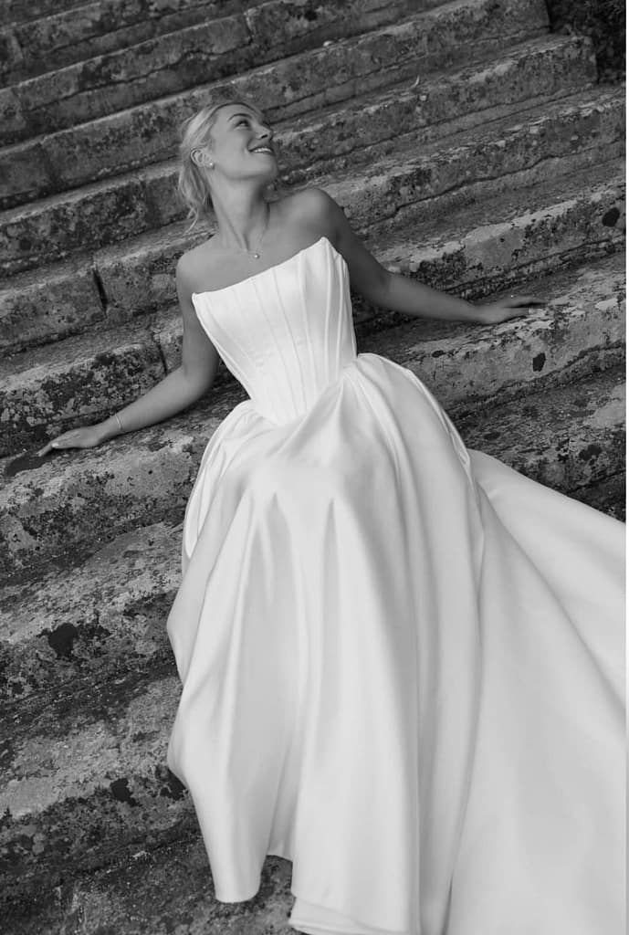 A black and white image of a bride sitting on brickwork steps leaning back, a pose for the photographer. Image promotes Lexi's destination weddings bridal makeup.
Lexi Brownfield - Bridal & Wedding Makeup Artist Essex.